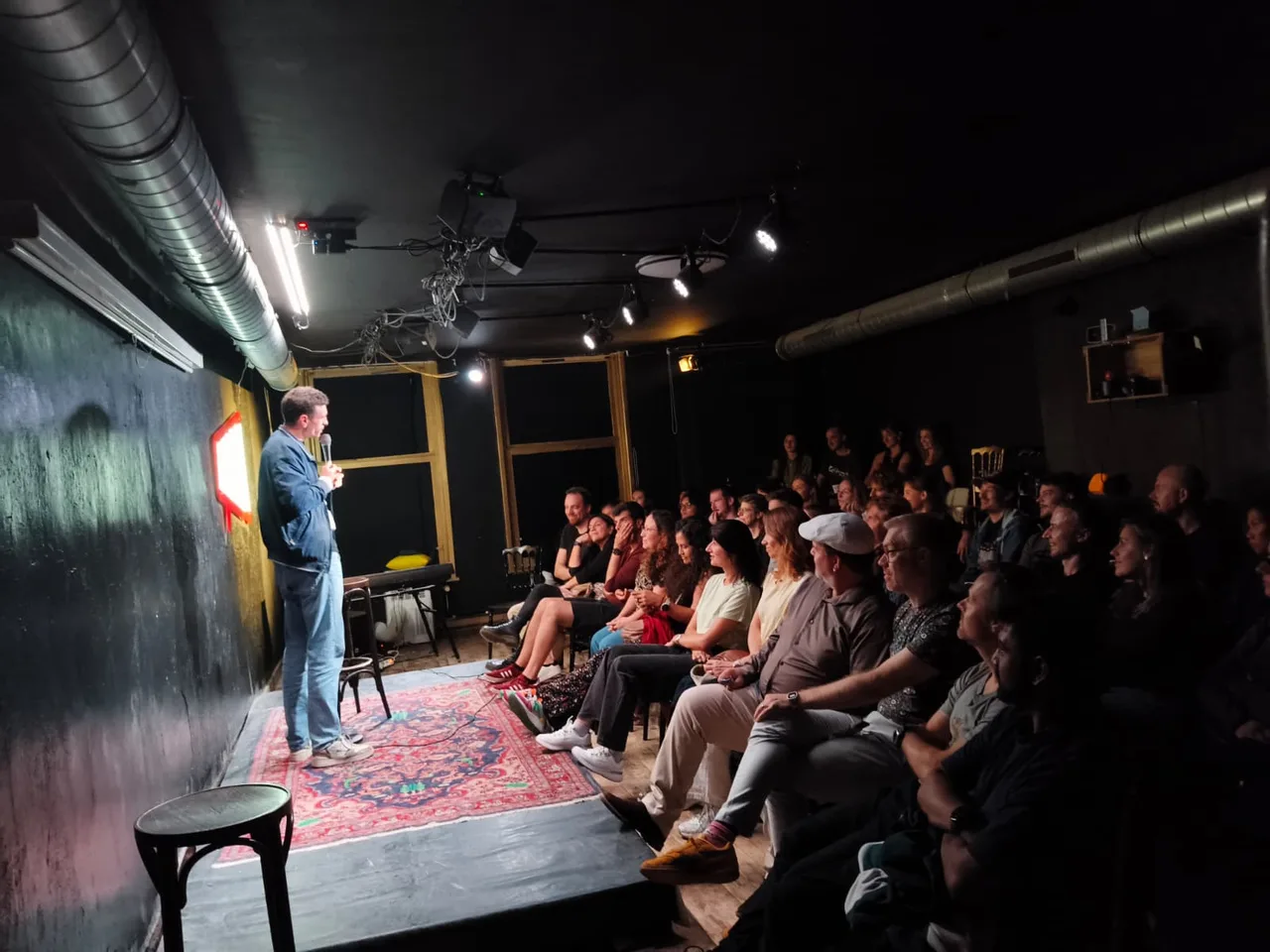 A comedian on the Amai stage with a smiling audience seated close by