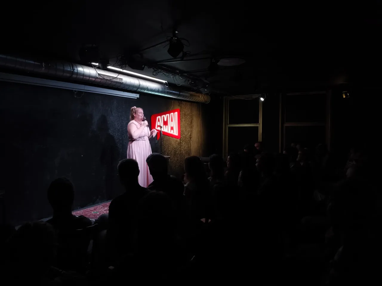 A comedian performing beside the red Amai sign in front of the audience